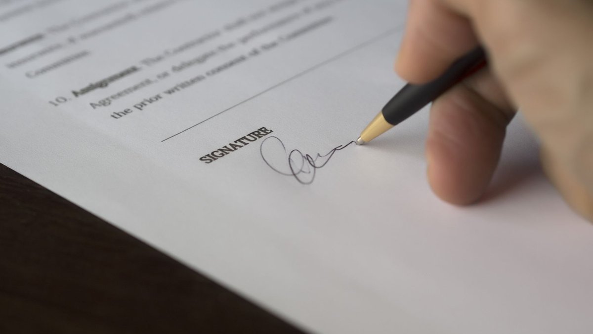 Person unterschreibt einen Arbeitsvertrag am Schreibtisch